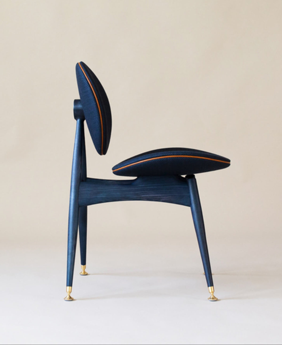 The side view of a modern dining chair featuring blue wood finished with a hardwax oil, leather and brass accents and a coordinating blue fabric.