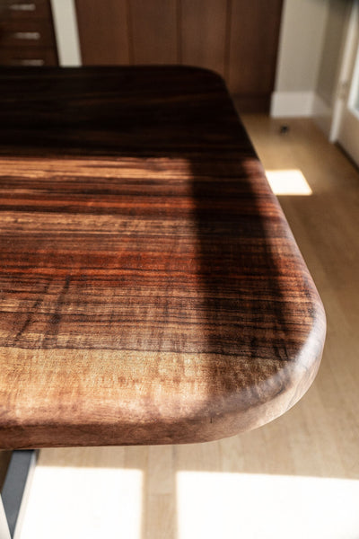 A claro walnut dining table with a rounded corner finished with a hardwax oil wood finish.