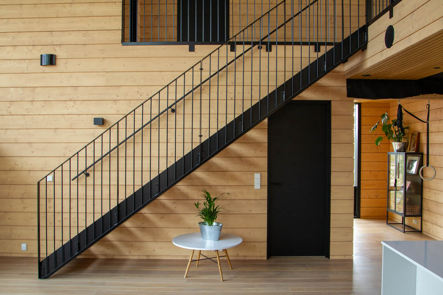A home with spruce wall cladding finished with Rubio Monocoat Oil Plus 2C. An iron staircase is in the center of the image along with various decor elements. 