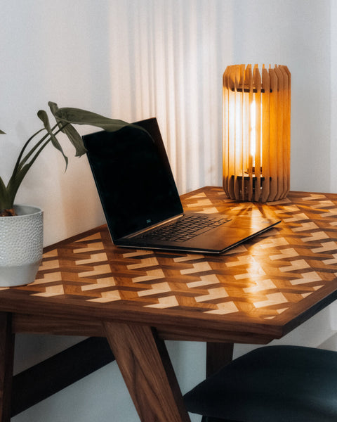 A contemporary wood desk with a computer, plant and lamp sitting on top of it. 