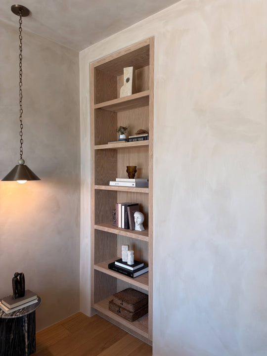 Floor-to-ceiling white oak bookcase in Rubio Monocoat Oil Plus 2C Natural, set into a plastered wall niche with brass pendant lighting.