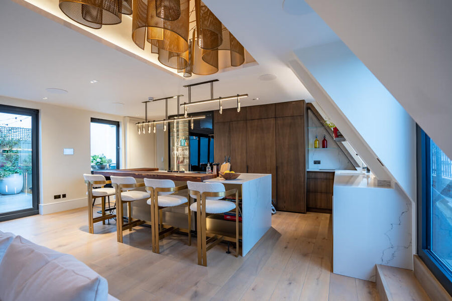 Four modern, luxurious barstools sit at an island made from white marble. The oak cabinetry provides a nice contrast against the light colored countertops. 