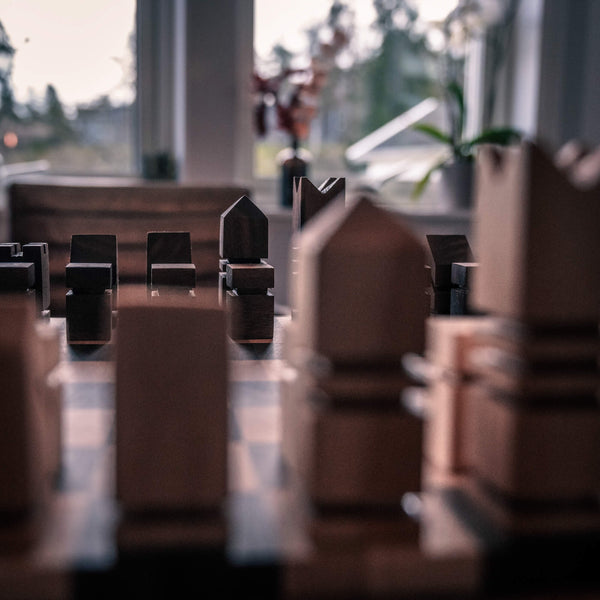 Maple chess pieces are out of focus in the foreground. In the background of the photos, handmade walnut chess pieces are pictured. 