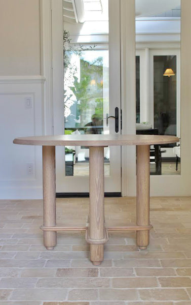 Round white oak table with four rounded legs and dimensional details. 