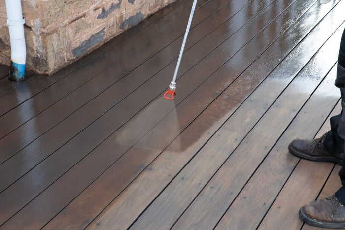 Painting contractor spraying exterior wood stain and finish on Cumaru deck boards.