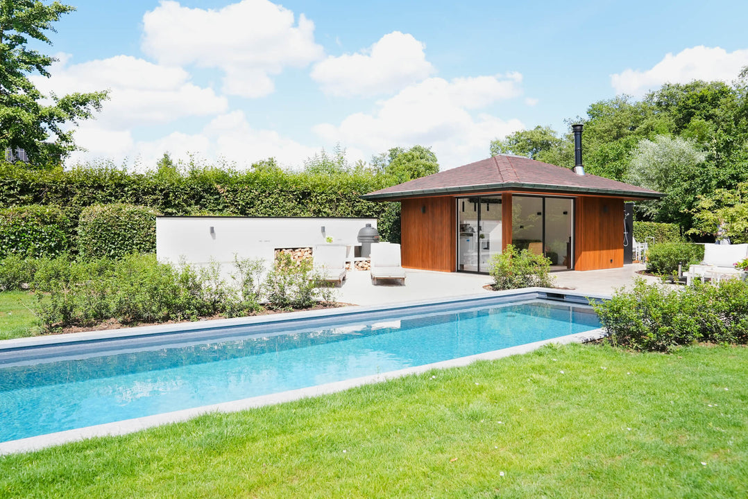 A bright blue inground pool is in the foreground of the image while a wood clad poolhouse finished using Rubio Monocoat DuroGrit is in the back.