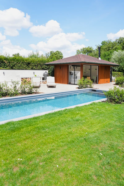 Green grass, an inground pool, and a poolhouse is pictured finished using a medium warm brown exterior wood finish called DuroGrit.