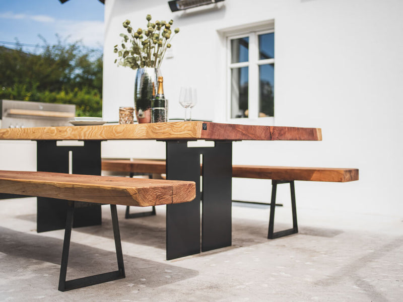 An outdoor redwood dining table top photographed at eye level with two benches on either side. Various dining elements adorn the top of the table.