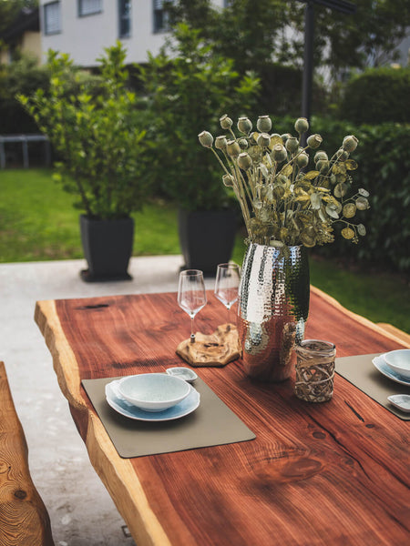 Two place settings and a vase with flowers sit atop a redwood dining table finished with Hybrid Wood Protector. 