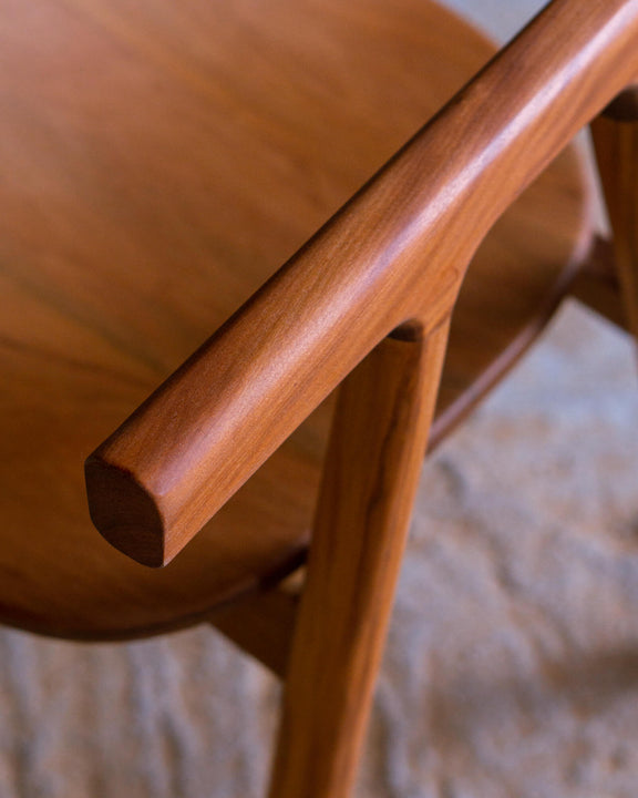 Close-up of the rounded armrest tip of a walnut chair, showcasing the hand-shaped end grain.