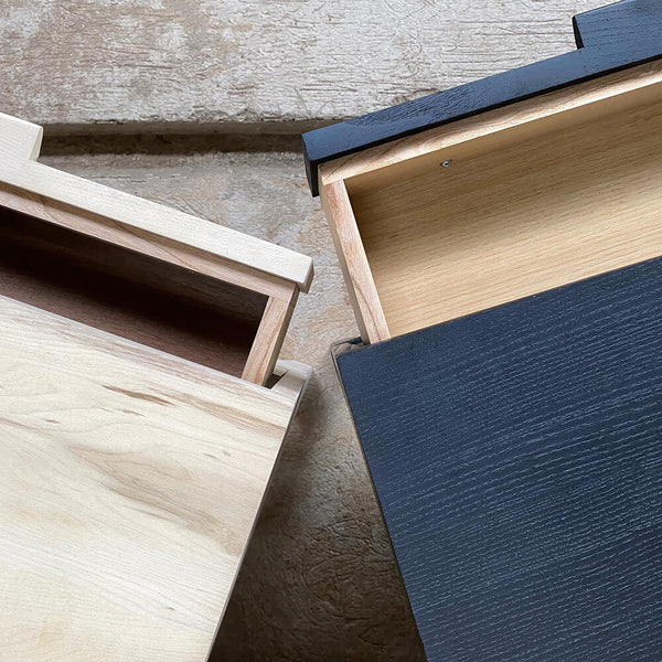 A light side table and a black side table side by side with the drawers partially open.