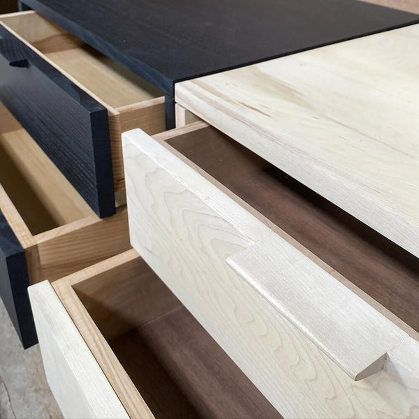 Two side tables, one black and one white side by side with two of their drawers partially open.