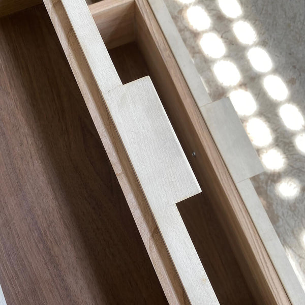 Two open walnut drawers on a maple nightstand with walnut interiors.