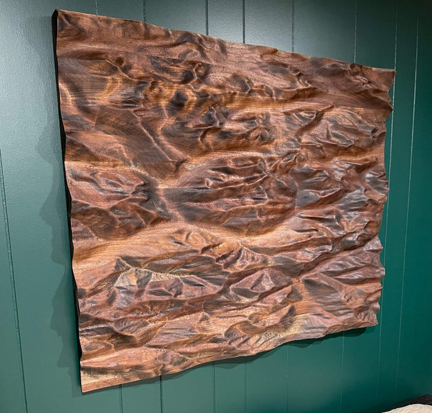 A walnut topographic map of the Canadian Rocky Mountains hanging on a green wall. 