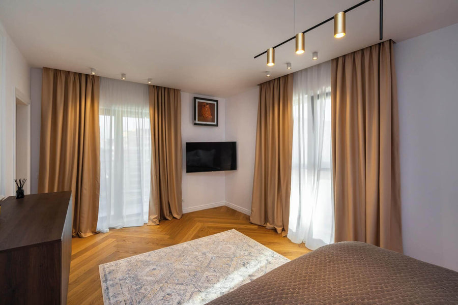 Herringbone wood floors in a living room with tall curtains around the windows.