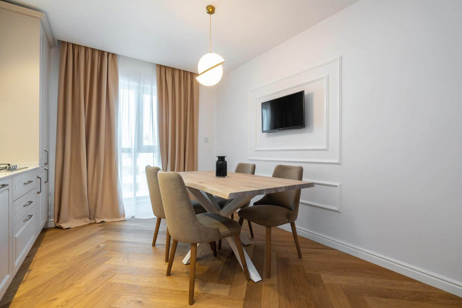 Dining area with tall windows, live edge table, white cabinets and a herringbone floor.