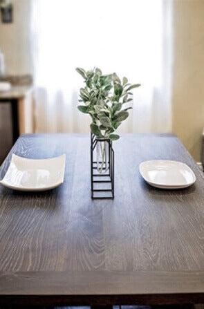 A wood dining table with 2 place settings and a plant in the middle.