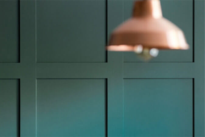 Close up of paneled teal wall with rose gold light fixture in foreground.