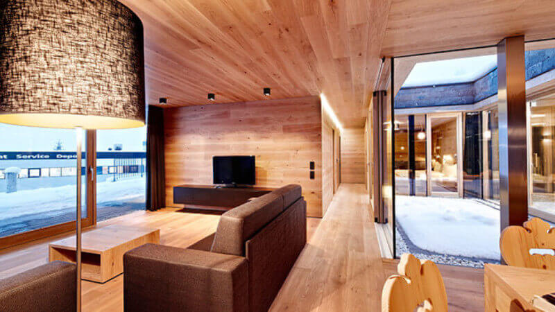 A lounge in a ski resort with all interior surfaces being oak wood and a couch overlooking the ski slopes.