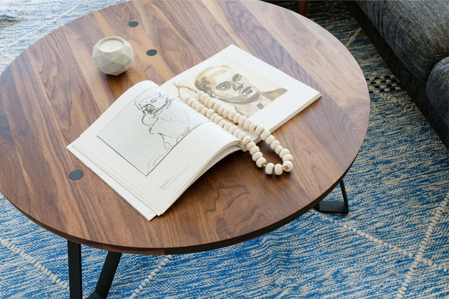Round walnut coffee table on blue rug with a book on it.