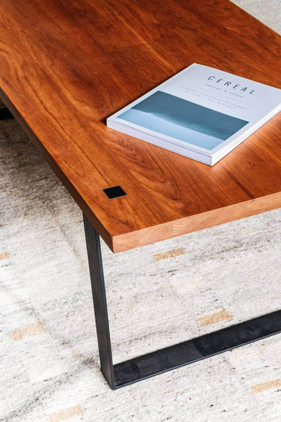 Beautiful modern style cherry wood coffee table on a rug with a book on it.