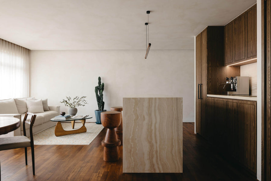 A view of wooden kitchen cabinets, stone waterfall island and a peak at the living area.