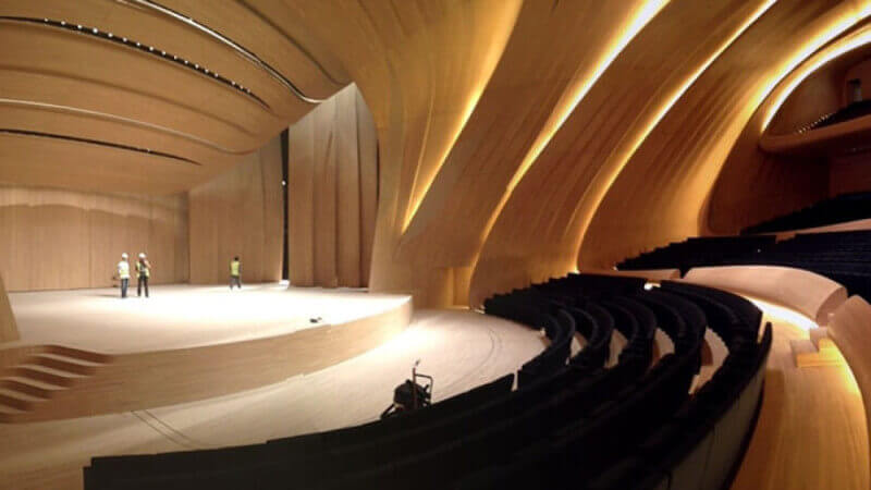 A large wood stage in an auditorium with seats curving around the front of the stage.