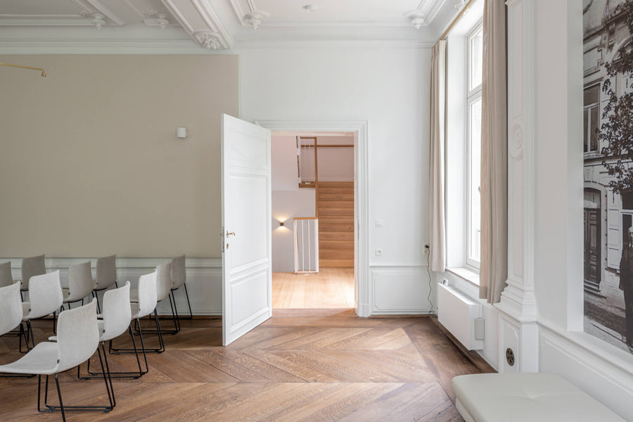 Gorgeous herringbone pattern wood flooring in a room with chairs and a door sitting open.