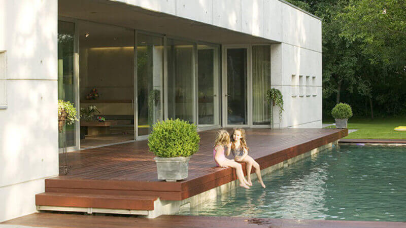 An oil finished Ipe deck beside a pool with 2 children soaking their feet in the pool.