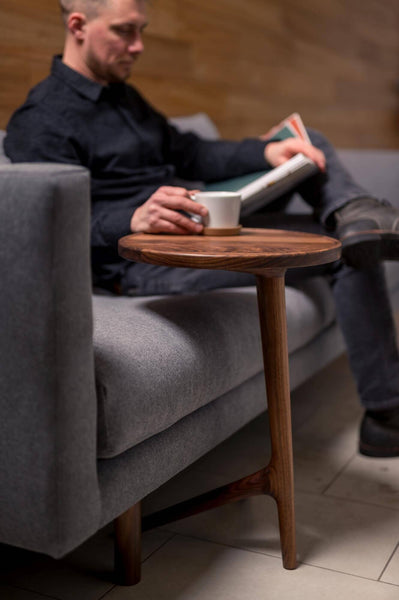 Man sitting on couch reading a book with his coffee on the couch table.