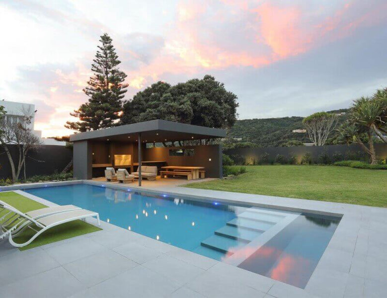 A pool in the backyard of a beach home with concrete decking and a pergola.