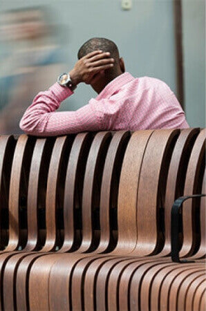 A man leaning on an oak wood bench seat with a tall back.