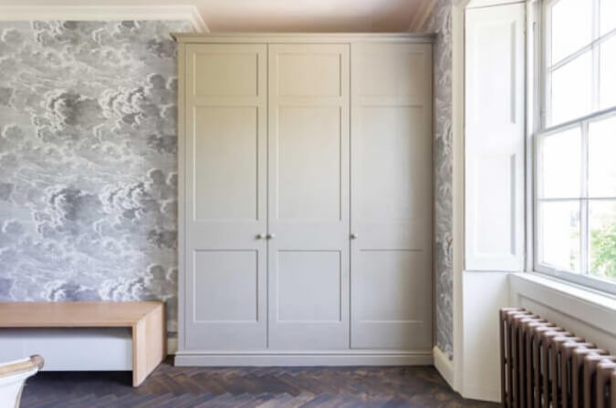 Wall sized wardrobe cabinets in a bedroom with herringbone wood flooring.