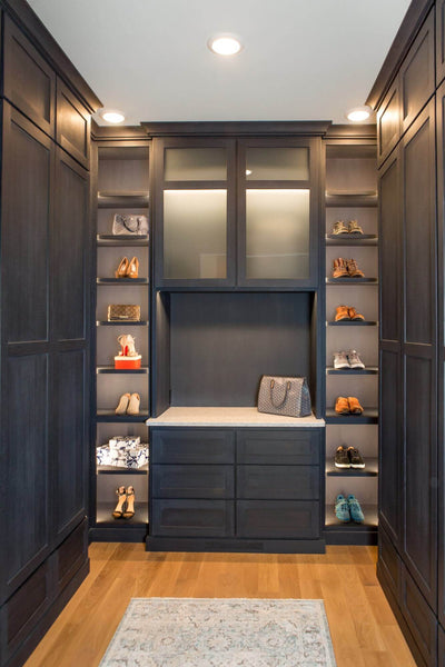 Luxury closet with shoe shelving, dark cabinetry and oak wood flooring.